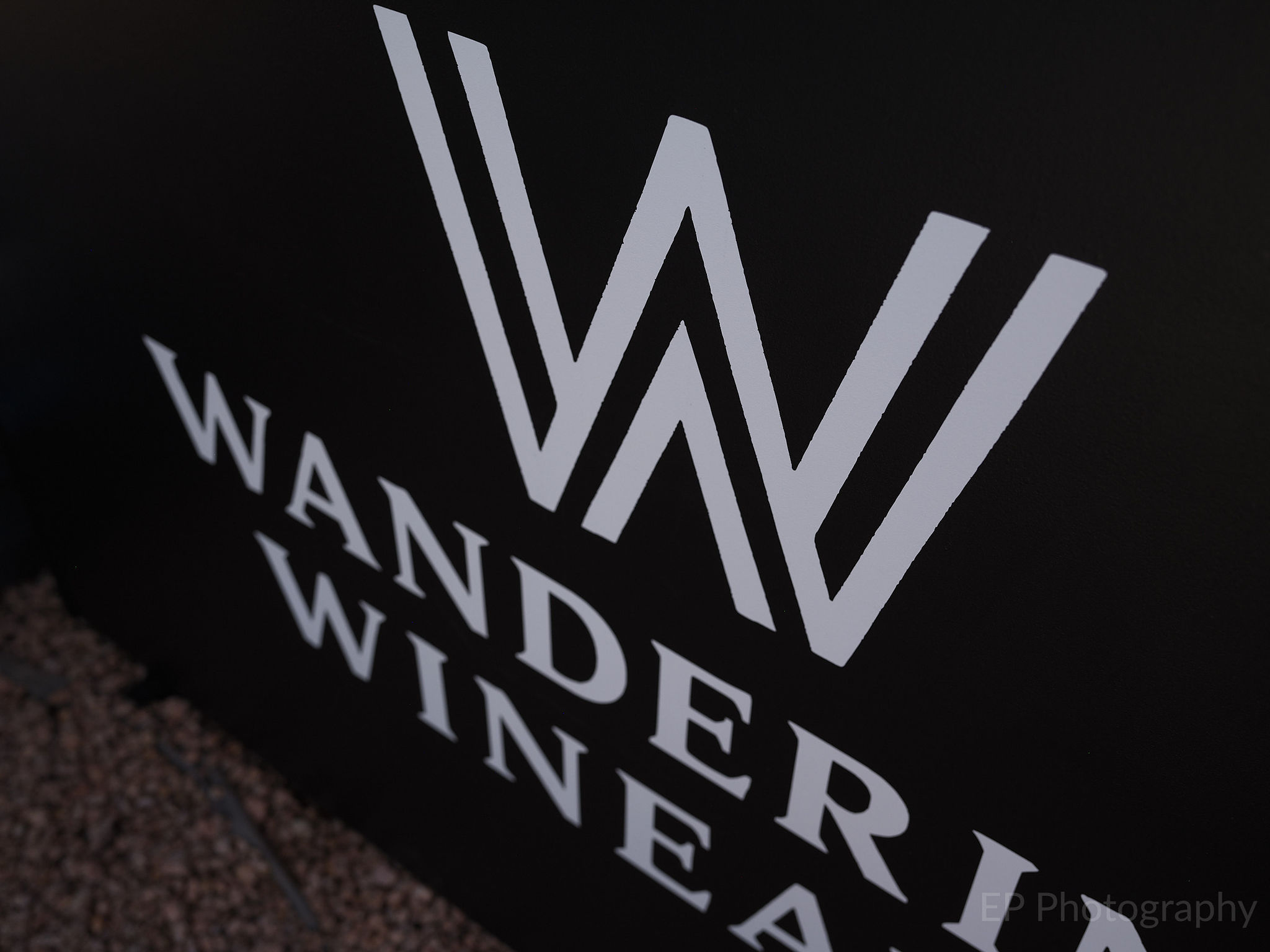 Close-up of The Wandering Wineaux logo on a black background, featuring a stylized 'W' design.